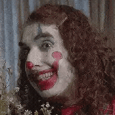 A Close Up Of A Woman Dressed As A Clown Holding Flowers . GIF