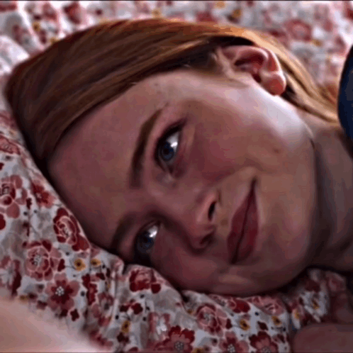 A Close Up Of A Woman Laying On A Bed With A Floral Comforter GIF