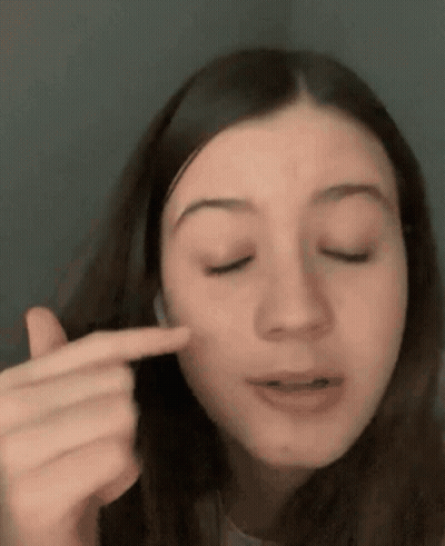 A Close Up Of A Woman Pointing At Her Face With Her Finger . GIF