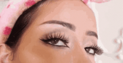 A Close Up Of A Woman 'S Eye With Long Eyelashes And A Pink Headband . GIF