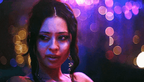 A Close Up Of A Woman 'S Face In A Dark Room With Purple Lights Behind Her . GIF