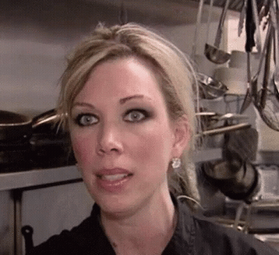 A Close Up Of A Woman 'S Face In A Kitchen With Pots And Pans Hanging From The Ceiling . GIF