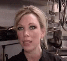 A Close Up Of A Woman 'S Face In A Kitchen With Pots And Pans Hanging On The Wall . GIF