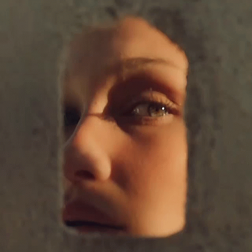A Close Up Of A Woman 'S Face Looking Through A Hole In A Wall GIF