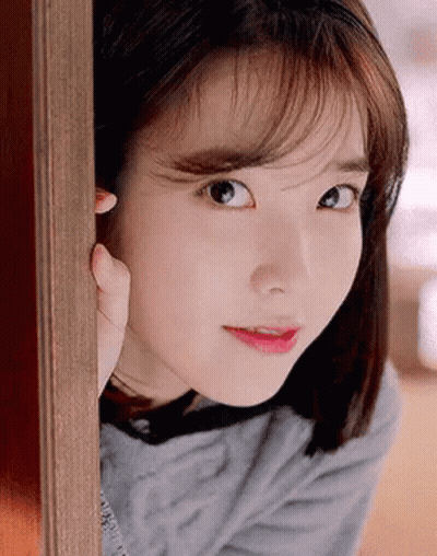 A Close Up Of A Woman 'S Face Peeking Out Of A Doorway . GIF