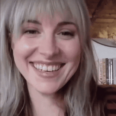 A Close Up Of A Woman 'S Face Smiling In Front Of A Bookshelf Filled With Books . GIF