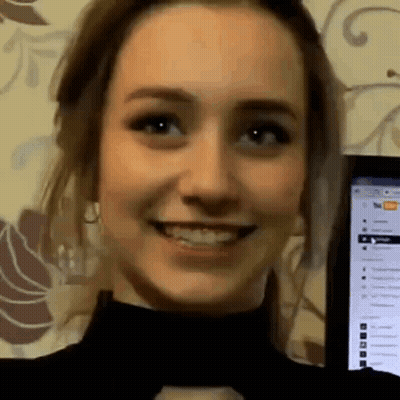 A Close Up Of A Woman 'S Face Smiling In Front Of A Computer Monitor . GIF