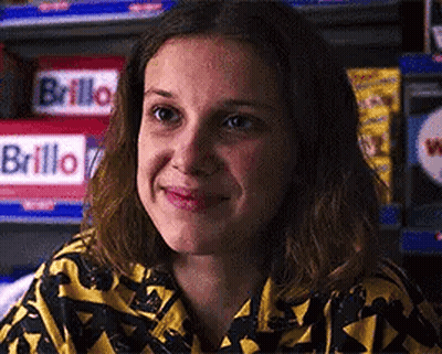A Close Up Of A Woman 'S Face Smiling In Front Of A Shelf . GIF