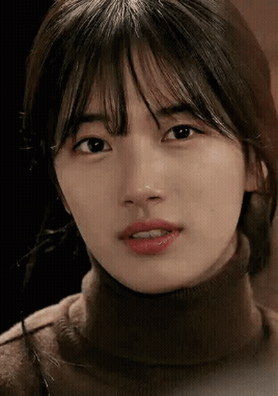 A Close Up Of A Woman 'S Face Wearing A Turtleneck Sweater And Looking At The Camera . GIF