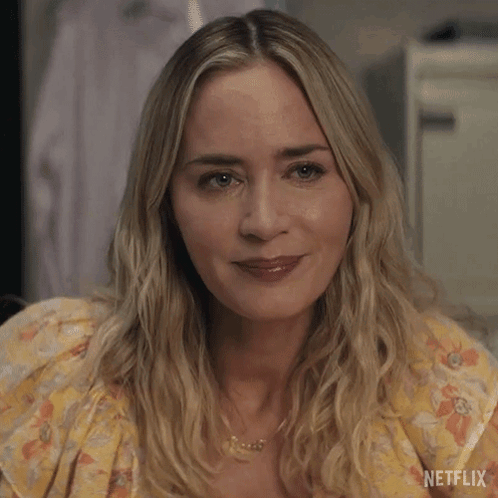 A Close Up Of A Woman 'S Face Wearing A Yellow Floral Dress And A Necklace . GIF