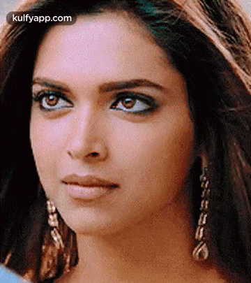 A Close Up Of A Woman 'S Face Wearing Earrings And A Blue Shirt . GIF