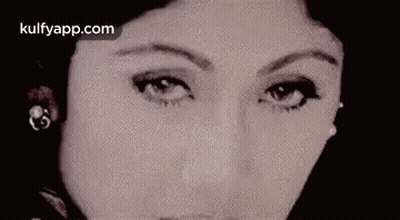 A Close Up Of A Woman 'S Face Wearing Earrings And Looking At The Camera . GIF