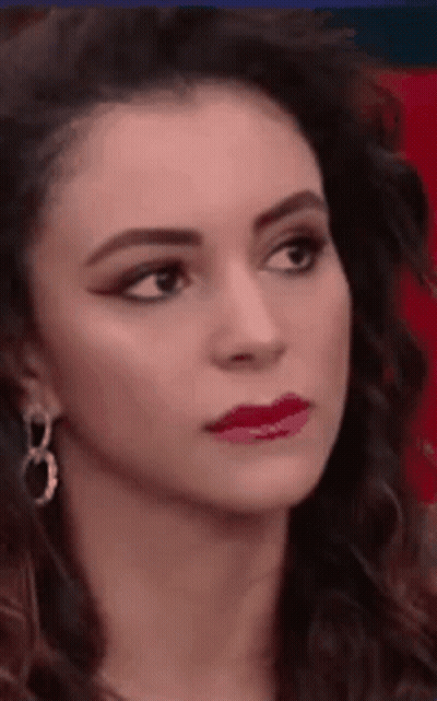 A Close Up Of A Woman 'S Face Wearing Earrings And Red Lipstick . GIF