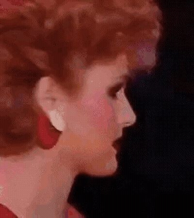 A Close Up Of A Woman 'S Face Wearing Red Earrings And Red Hair . GIF