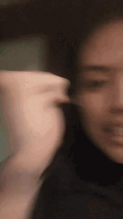 A Close Up Of A Woman 'S Face With A Blurry Background And A Hand Behind Her Ear . GIF