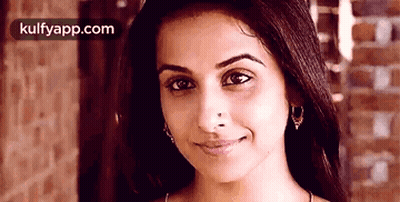 A Close Up Of A Woman 'S Face With A Brick Wall In The Background And Kulfyapp.com In The Corner GIF
