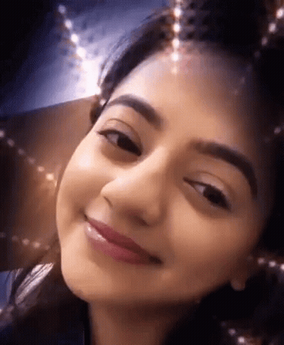 A Close Up Of A Woman 'S Face With A Christmas Tree In The Background GIF