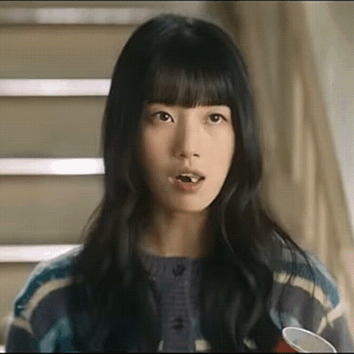 A Close Up Of A Woman 'S Face With A Cup In Her Hand And Stairs In The Background . GIF