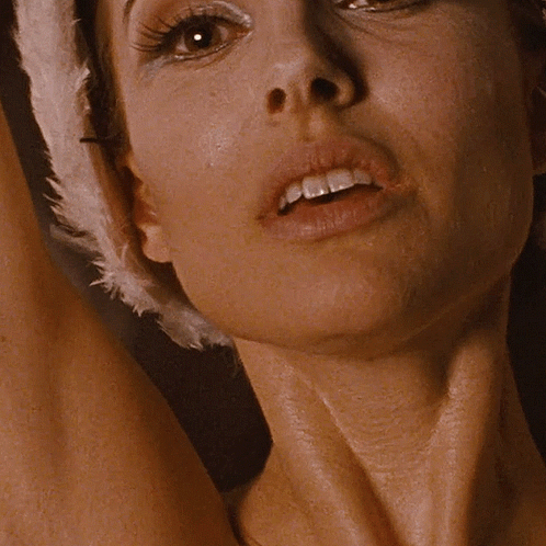 A Close Up Of A Woman 'S Face With A Feathered Hat On Her Head GIF