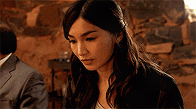 A Close Up Of A Woman 'S Face With A Man In A Suit In The Background GIF