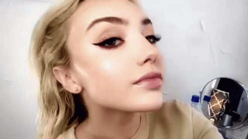 A Close Up Of A Woman 'S Face With A Mirror Behind Her . GIF