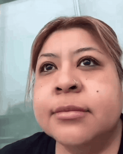 A Close Up Of A Woman 'S Face With A Nose Ring And A Black Shirt . GIF