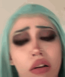 A Close Up Of A Woman 'S Face With A Nose Ring And Blue Hair . GIF