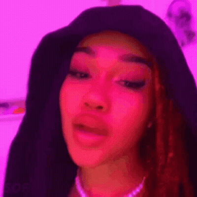 A Close Up Of A Woman 'S Face With A Pink Background And A Purple Hat . GIF