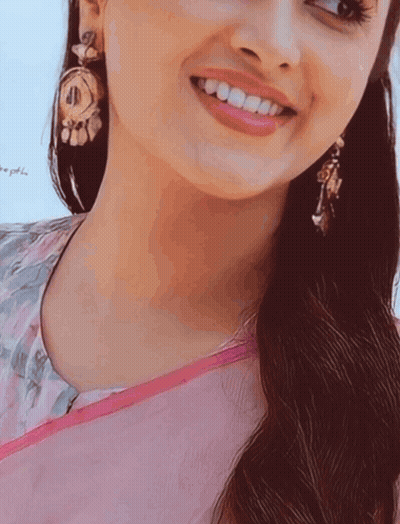 A Close Up Of A Woman 'S Face With A Pink Shirt And Earrings GIF
