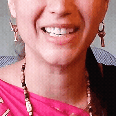A Close Up Of A Woman 'S Face With A Pink Shirt And Earrings With Keys On Them GIF