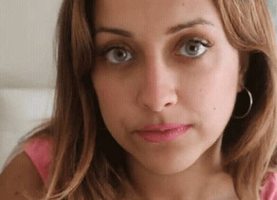A Close Up Of A Woman 'S Face With A Pink Shirt And Hoop Earrings . GIF