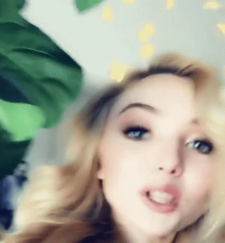 A Close Up Of A Woman 'S Face With A Plant In The Background GIF