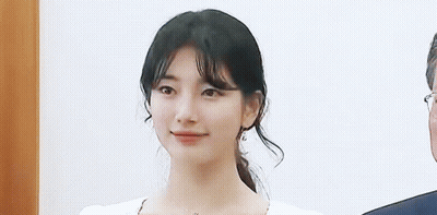 A Close Up Of A Woman 'S Face With A Ponytail And A Man In A Suit Behind Her . GIF
