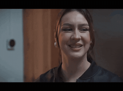 A Close Up Of A Woman 'S Face With A Ponytail And Earrings Smiling . GIF