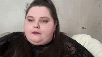 A Close Up Of A Woman 'S Face With A Ponytail And Pink Earrings . GIF