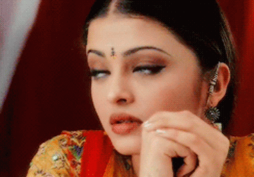 A Close Up Of A Woman 'S Face With A Red Curtain Behind Her GIF