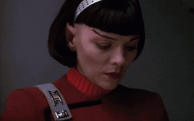A Close Up Of A Woman 'S Face With A Red Sweater And A Strap That Says Xtc On It GIF