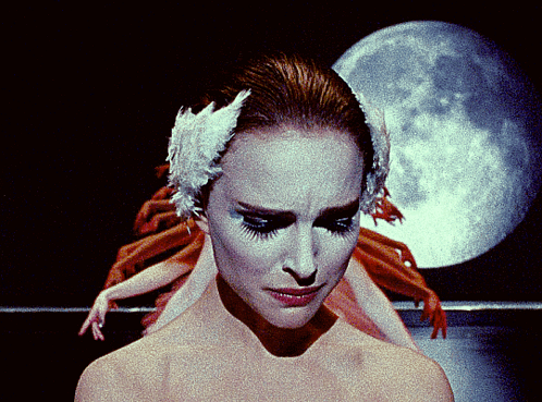 A Close Up Of A Woman 'S Face With A Swan Feather In Her Hair GIF