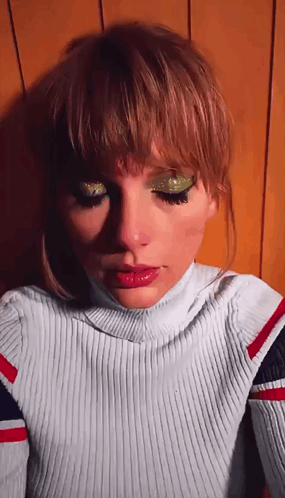 A Close Up Of A Woman 'S Face With A Turtleneck And Green Eyeshadow GIF