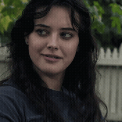 A Close Up Of A Woman 'S Face With A White Picket Fence Behind Her GIF