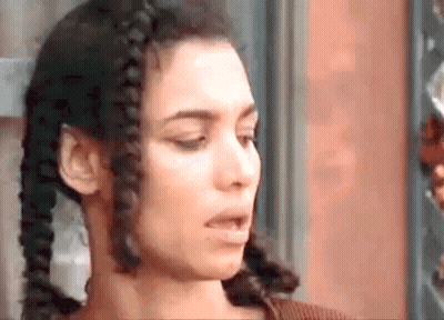 A Close Up Of A Woman 'S Face With Braids In Her Hair Making A Funny Face . GIF