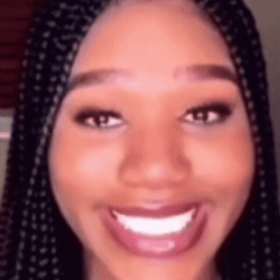 A Close Up Of A Woman 'S Face With Braids Smiling And Looking At The Camera . GIF