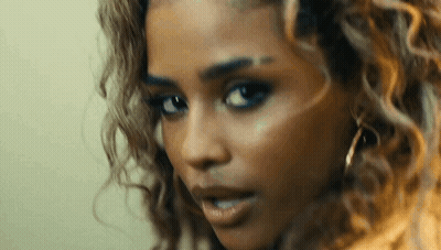 A Close Up Of A Woman 'S Face With Curly Hair And Earrings Looking At The Camera . GIF