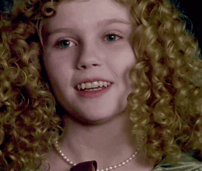 A Close Up Of A Woman 'S Face With Curly Hair Wearing A Pearl Necklace GIF