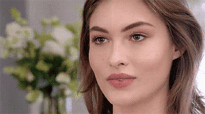 A Close Up Of A Woman 'S Face With Flowers In The Background . GIF