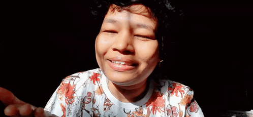 A Close Up Of A Woman 'S Face With Her Eyes Closed And A Floral Shirt . GIF