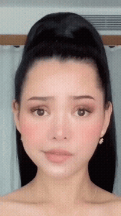 A Close Up Of A Woman 'S Face With Her Hair In A Bun And Earrings . GIF