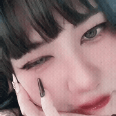 A Close Up Of A Woman 'S Face With Her Hand On Her Face And A Black Nail . GIF