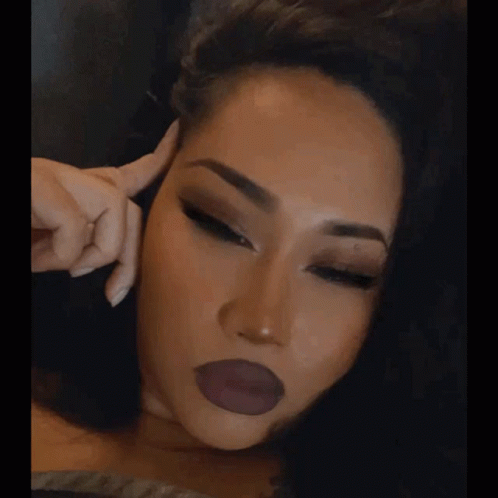 A Close Up Of A Woman 'S Face With Her Hand On Her Forehead GIF