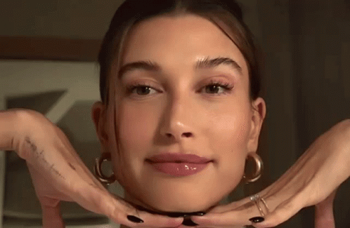 A Close Up Of A Woman 'S Face With Her Hands Making A Face . GIF